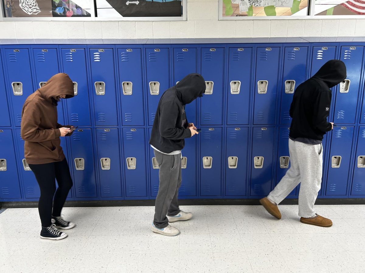 Three students slumped over looking at their cell phones. Photo by Fred Avett.