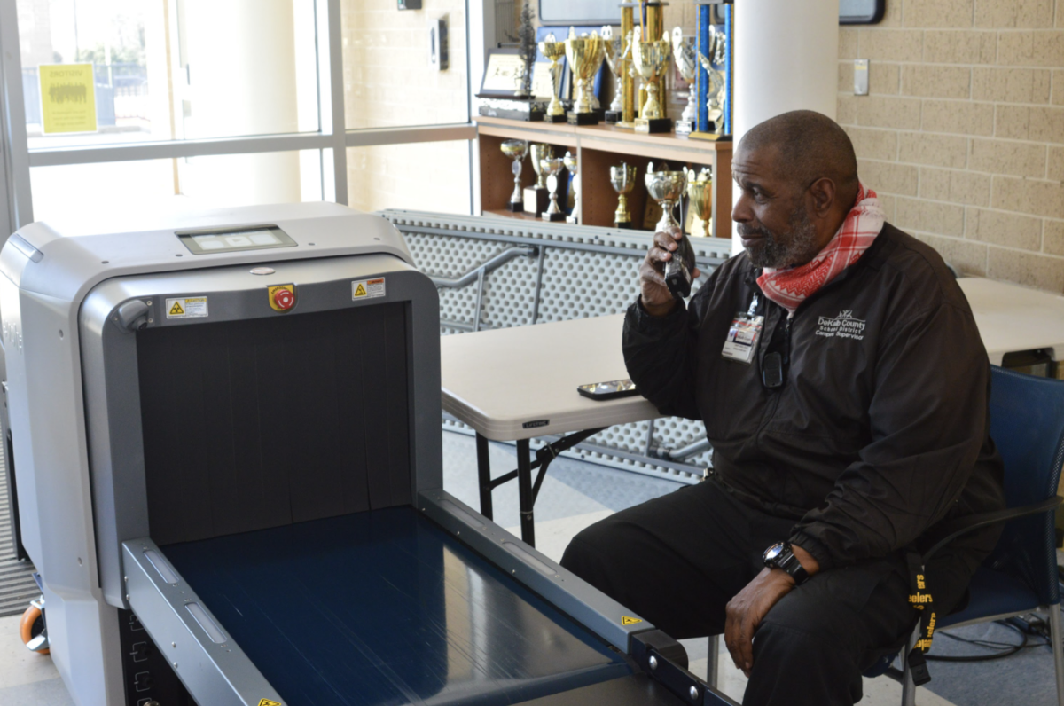 Officer Umar Abdul-Alim posing on his walkie-talkie by the new weapons detector. Photo by Finley Malone.